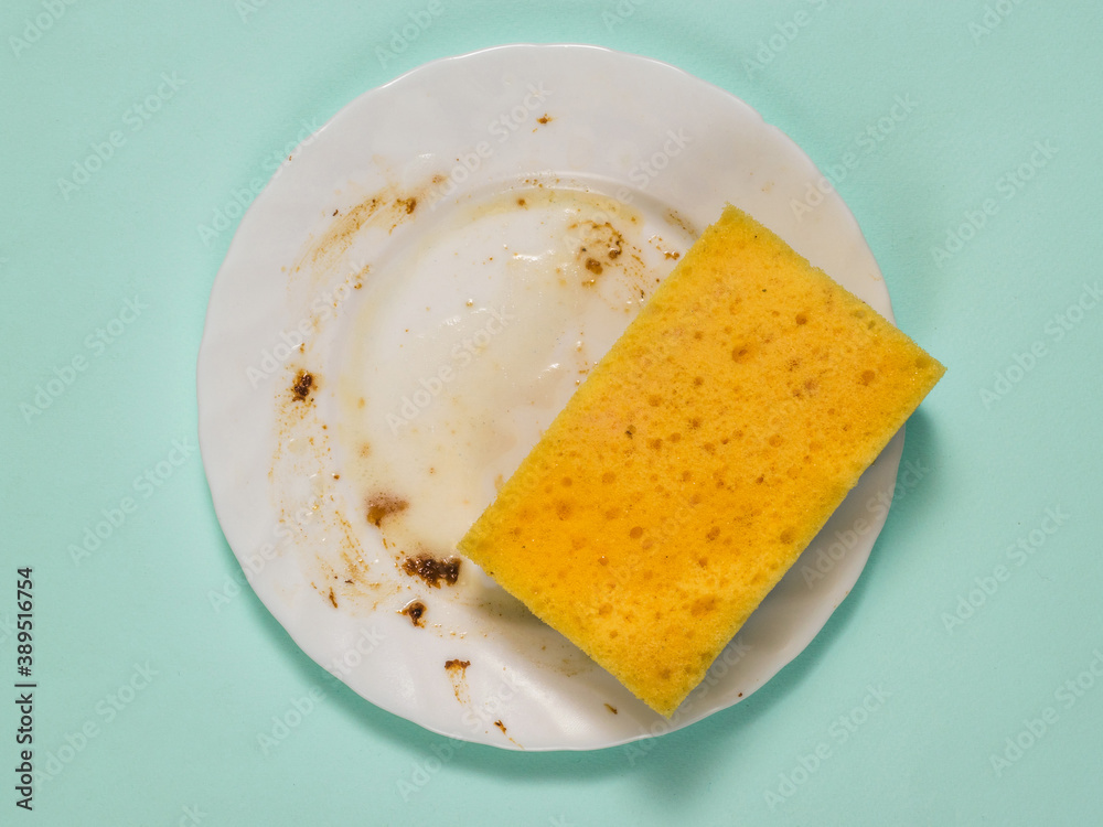 Sponge with detergent on a dirty plate on a blue background.