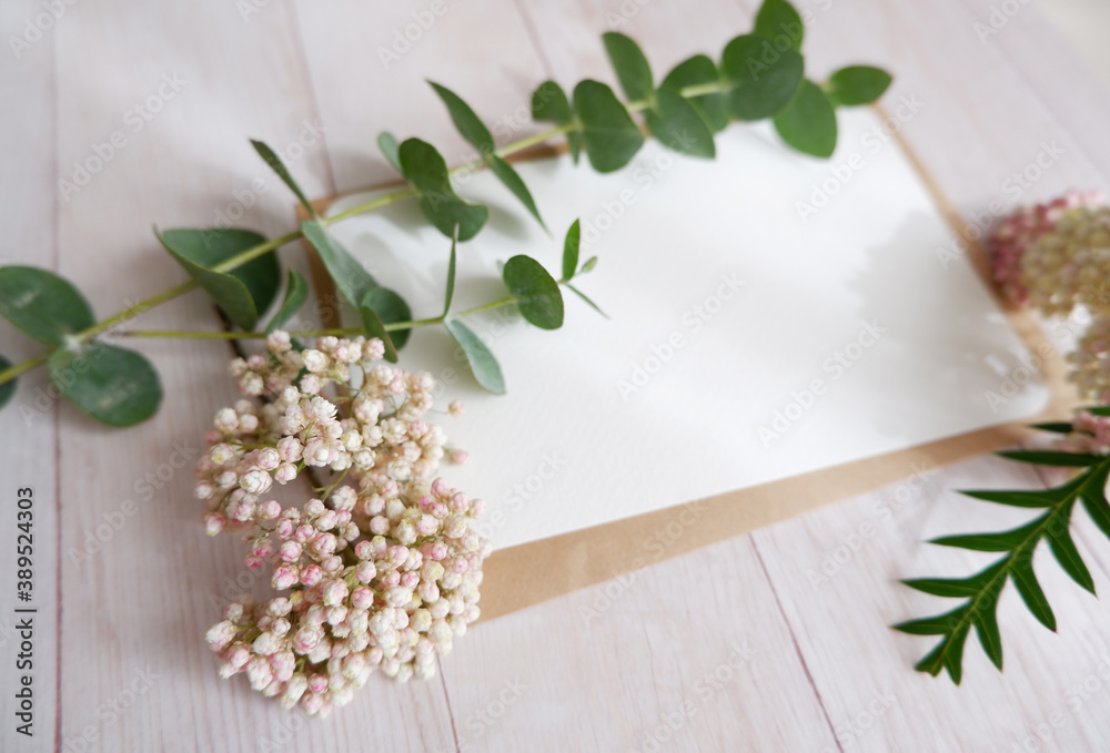 Empty card with flowers and green leaves on wooden background. ウッドテーブルを背景にカードと白い花と緑ドライフワラー
