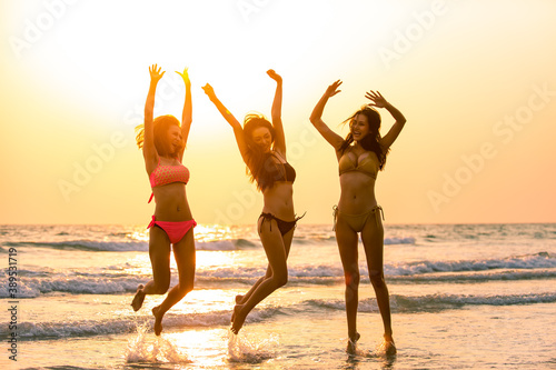 Group of Happy young beautiful Asian women in bikini swimwear playing and jumping together on the beach at sunset. Three sexy girl friends relax and having fun in summer holidays vacation travel