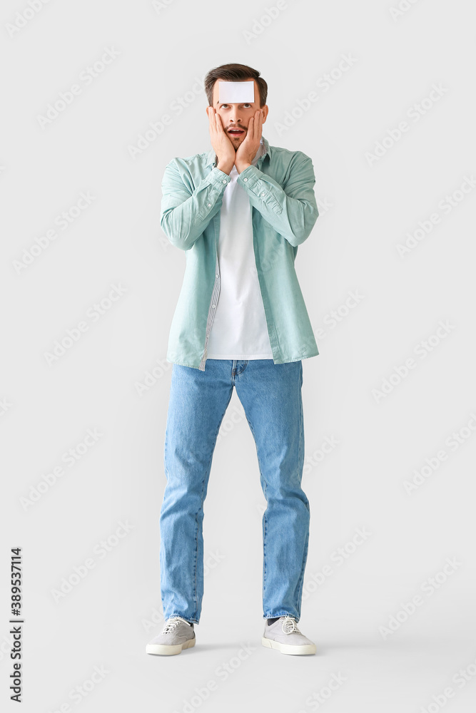 Fototapeta premium Confused man with blank note paper on his forehead against grey background