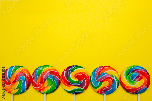 Bright swirl lollipops on yellow background with copy space. Festive background with colorful twisted candies.