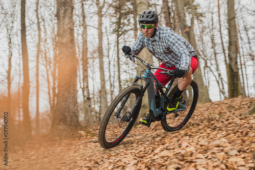 Hipster biker charging downhill with a modern lightweight electric bicycle or mountain bike in autumn or winter setting in a forest.