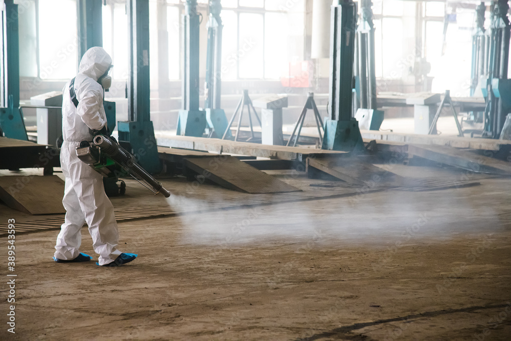Worker in a protective suit handles industrial premises, buildings, and interiors to protect against COVID-19 infection. Coronavirus