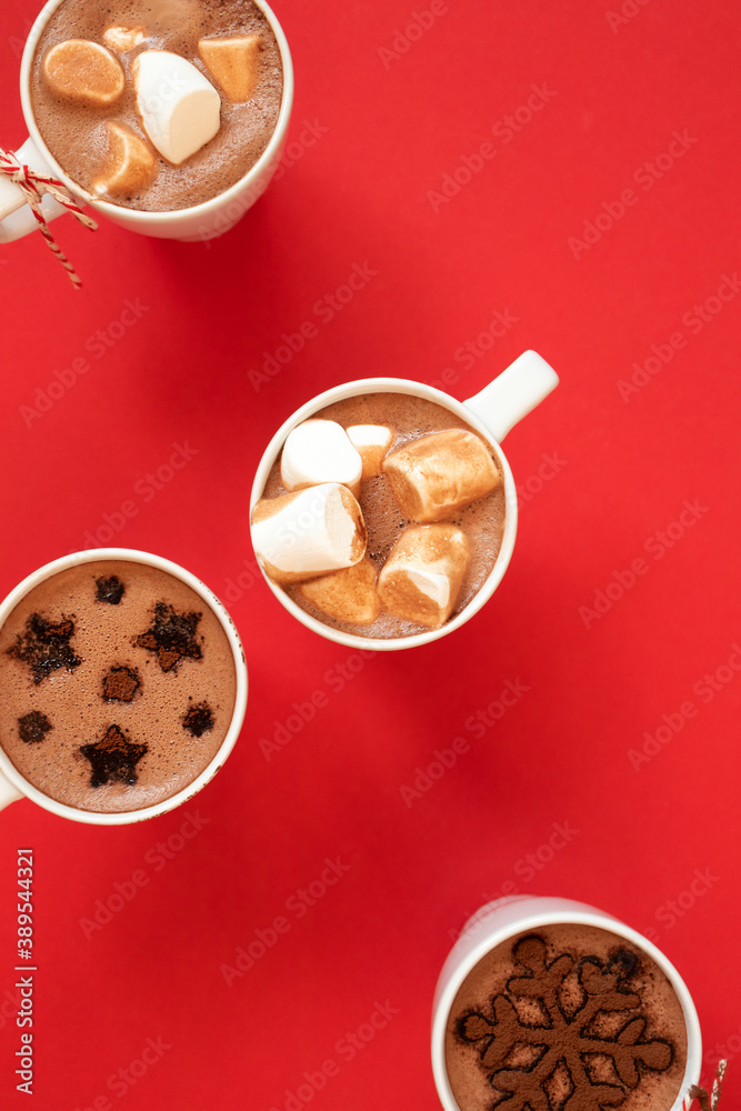 White cups with hot cocoa and marshmallows and spice cinnamon decor on red background, vertical. Winter holidays drinks concept White cups with hot cocoa and marshmallows and spice cinnamon decor on red background, vertical. Winter holidays drinks concept