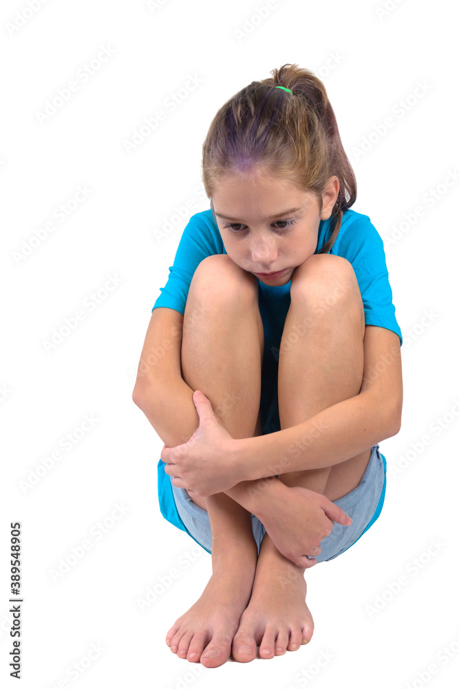 A sad and upset girl in blue shirt with hands wrapped around her knees sitting on the floor A sad and upset girl in blue shirt with hands wrapped around her knees sitting on the floor
