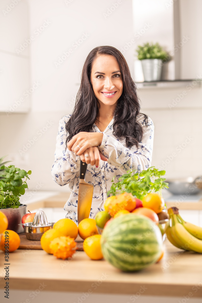 Smiling girl holds a knife in the kitchen surrounded by fresh fruit and herbs Smiling girl holds a knife in the kitchen surrounded by fresh fruit and herbs