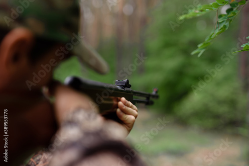Hunter Aiming with Shotgun in Summer Forest.