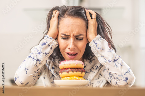 Woman holding her head by hands over irresistable pile of donuts
