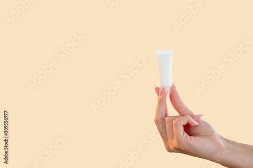 Cosmetic product. Skin care. Body treatment. Minimal presentation of white mockup tube with lotion in female hand isolated on pastel peach color copy space commercial background. © golubovy