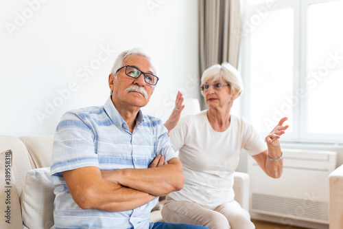 Angry elderly woman arguing with her husband. Senior couple having difficulty in marriage. Old couple sitting on the sofa at home