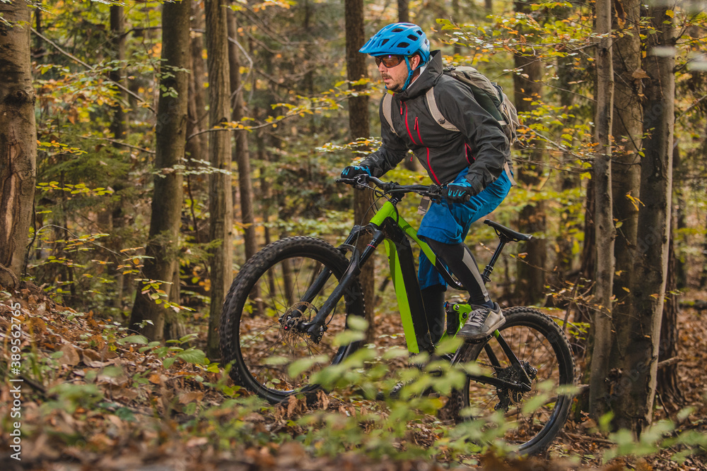 Biker riding uphill with a modern electric bicycle or mountain bike in autumn or winter setting in a forest. Modern e-cyclist in woods. Biker riding uphill with a modern electric bicycle or mountain bike in autumn or winter setting in a forest. Modern e-cyclist in woods.