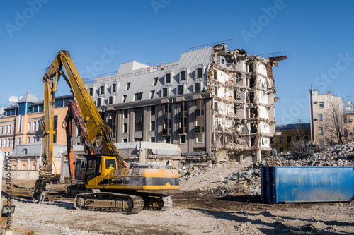 Construction machines near multi-storey building without walls and bare load-bearing structures, gradually destroyed for demolition