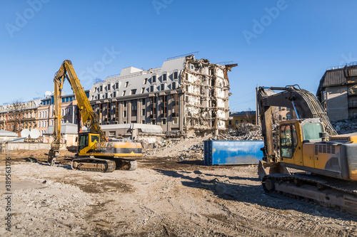 Construction machines near multi-storey building without walls and bare load-bearing structures, gradually destroyed for demolition