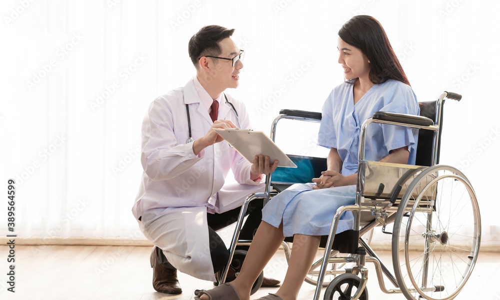 Patient on wheelchair visiting doctor for regular check. Smiling doctor explaining checkup information talking in front of a patient on a wheelchair. Healthcare workers in the Coronavirus, Covid19.