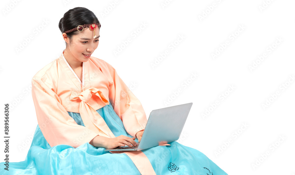 Attractive woman wearing traditional Korean Hanbok dress. Young Woman wearing a traditional Hanbok using computer notebook. Traditional and Technology concept. Attractive woman wearing traditional Korean Hanbok dress. Young Woman wearing a traditional Hanbok using computer notebook. Traditional and Technology concept.