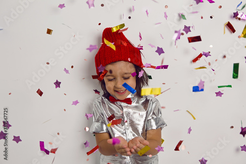 Christmas portrait in a knitted hat of a boy child in a silver shirt and red bow tie catches glitter confetti on holiday