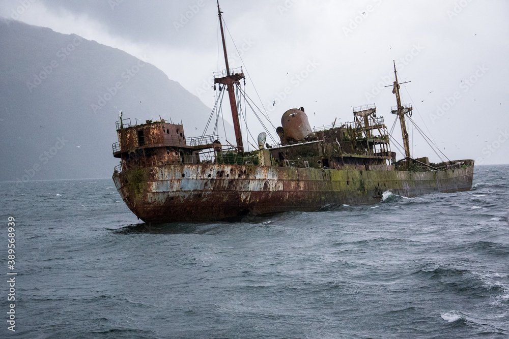 épave d'un bateau rouillé et abandonné depuis des années ayant eu une avarie, semblant naviguer seul sur les eaux tel un vaisseau fantôme  