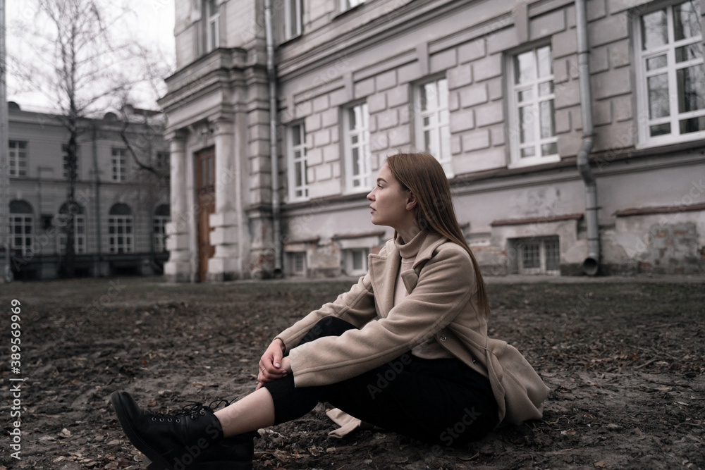 sad student sitting on cold ground against the background of an educational institution, cold autumn, winter, expulsion, closed building in quarantine, distance learning