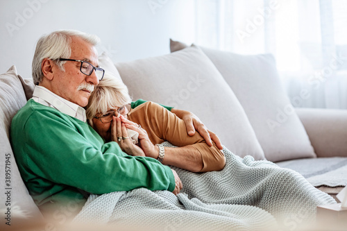 Elderly man and woman with flu. Couple of old aged senior people at home with seasonal winter cold illness disease sit down on the sof together forever - health problems for retired man and woman  photo