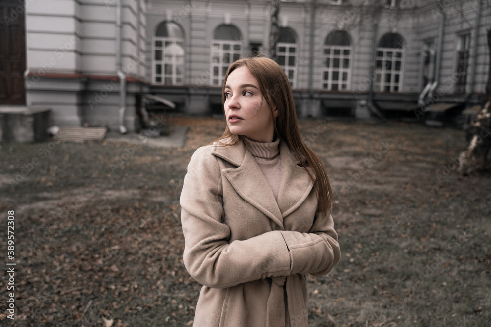 Fototapeta premium a girl warms her hands in her sleeves, a beautiful girl stands in a field dressed in a coat