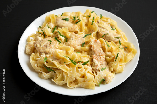 Homemade Chicken Fettuccine Alfredo on a white plate on a black background, low angle view.