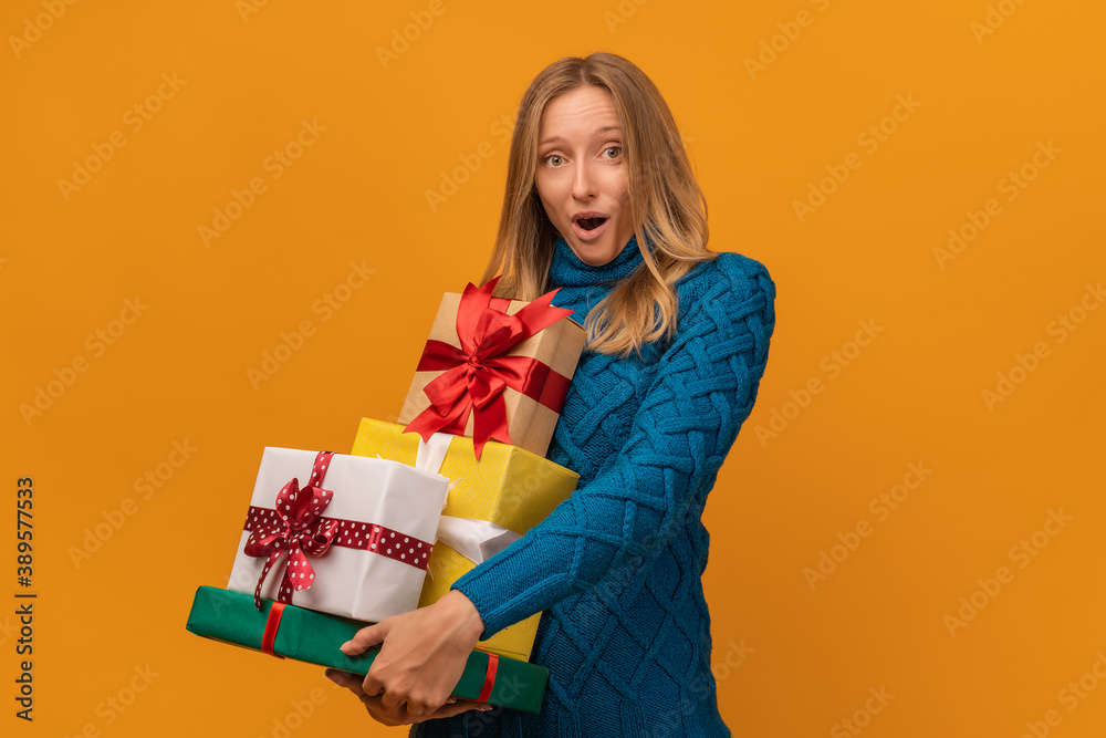 Portrait of a charming young woman in knitted sweater holding stack of present boxes. Studio shot, yellow background Portrait of a charming young woman in knitted sweater holding stack of present boxes. Studio shot, yellow background