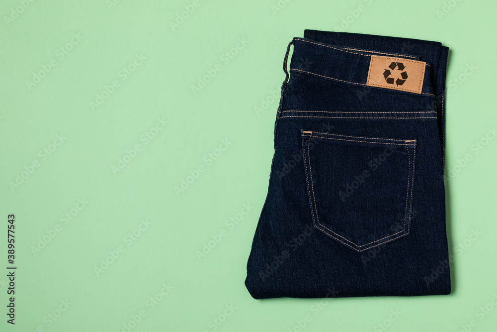 Recycled blue jeans with a clothing tag. Circular economy logo, zero waste  concept. Reusing materials and reducing waste in fashion. Denim horizontal  flat lay shot on a green background foto de Stock