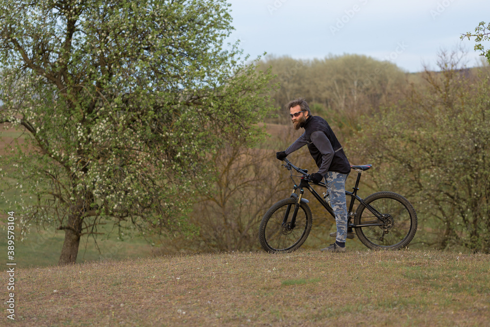 Sports brutal bearded guy on a modern mountain bike. Cyclist on the green hills in the spring. Sports brutal bearded guy on a modern mountain bike. Cyclist on the green hills in the spring.