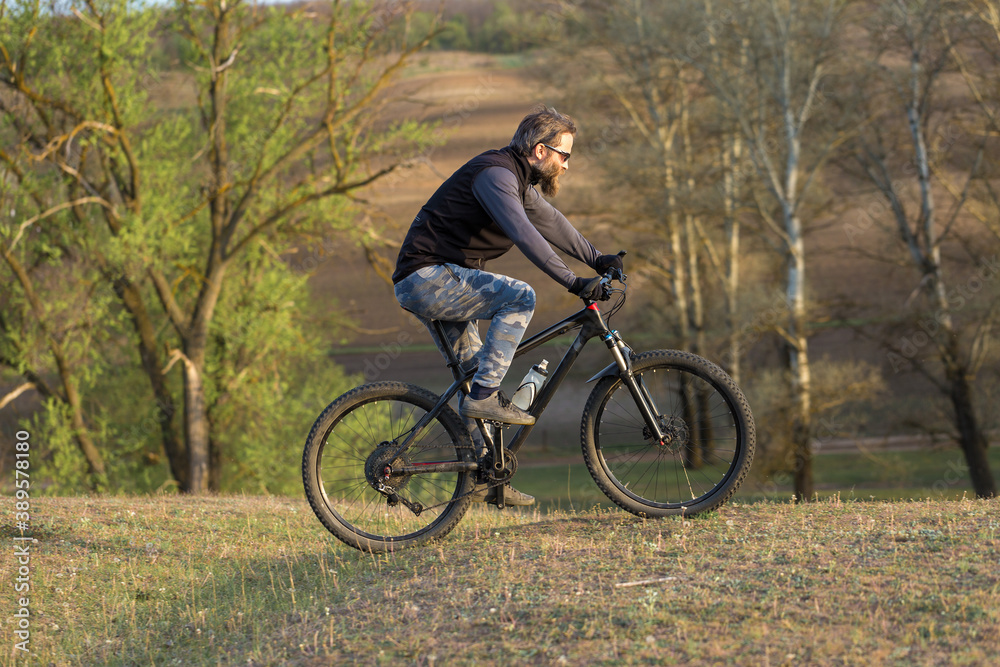 Sports brutal bearded guy on a modern mountain bike. Cyclist on the green hills in the spring. Sports brutal bearded guy on a modern mountain bike. Cyclist on the green hills in the spring.