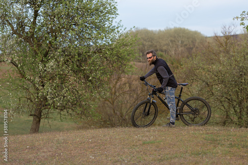 Sports brutal bearded guy on a modern mountain bike. Cyclist on the green hills in the spring. © Mountains Hunter