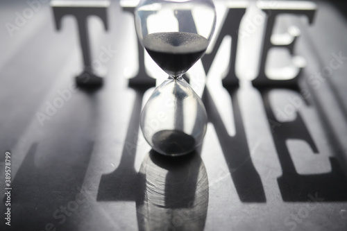 The concept of the passage of time. Hourglass on a dark background. Inscription time. The shadow on the surface of the word.