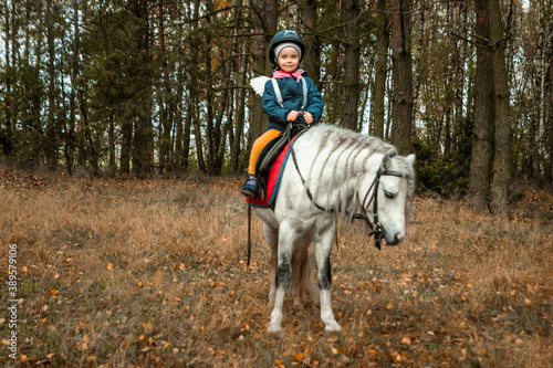 Little girl on a white pony on a background of nature. Jockey, hippodrome, horseback riding.