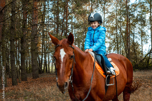 Little girl on an adult brown horse on the background of nature. Jockey, epodrome, horseback riding.