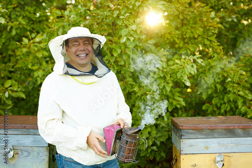 young diligent caucasian adult man beekeeper work with bee smoker in his apiary on bee farm, wearing whute uniform