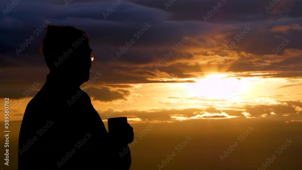 Side view of Asian senior drinking hot coffee outdoor and enjoying the beautiful sky landscape at sunset on the mountain top.