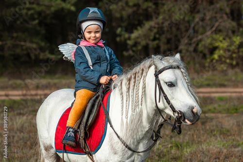 Little girl on a white pony on a background of nature. Jockey, hippodrome, horseback riding.