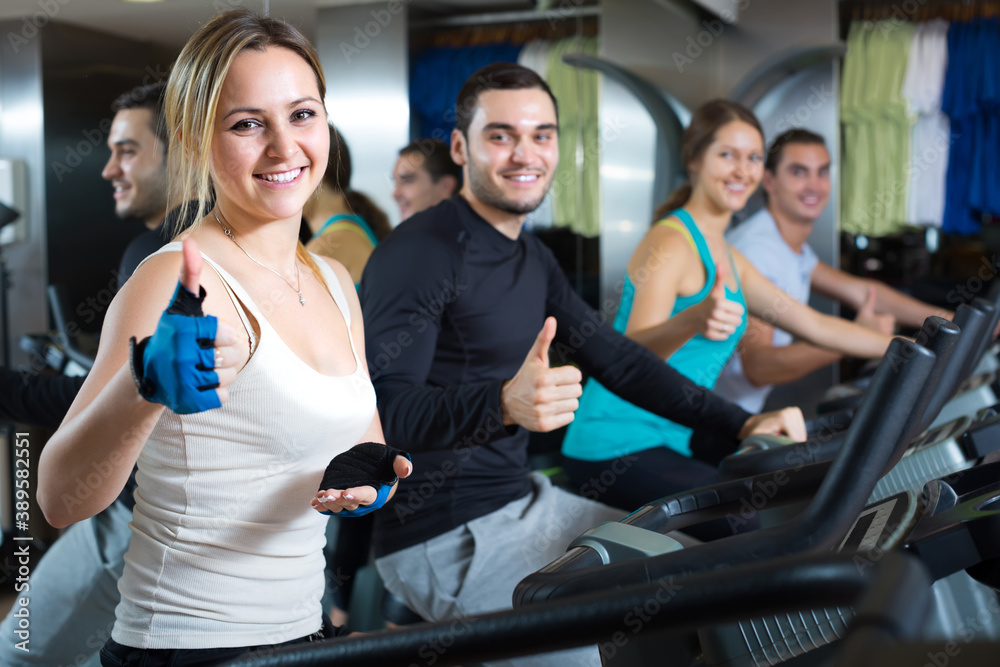 Fototapeta premium Smiling active young adults training on exercise bikes in gym.