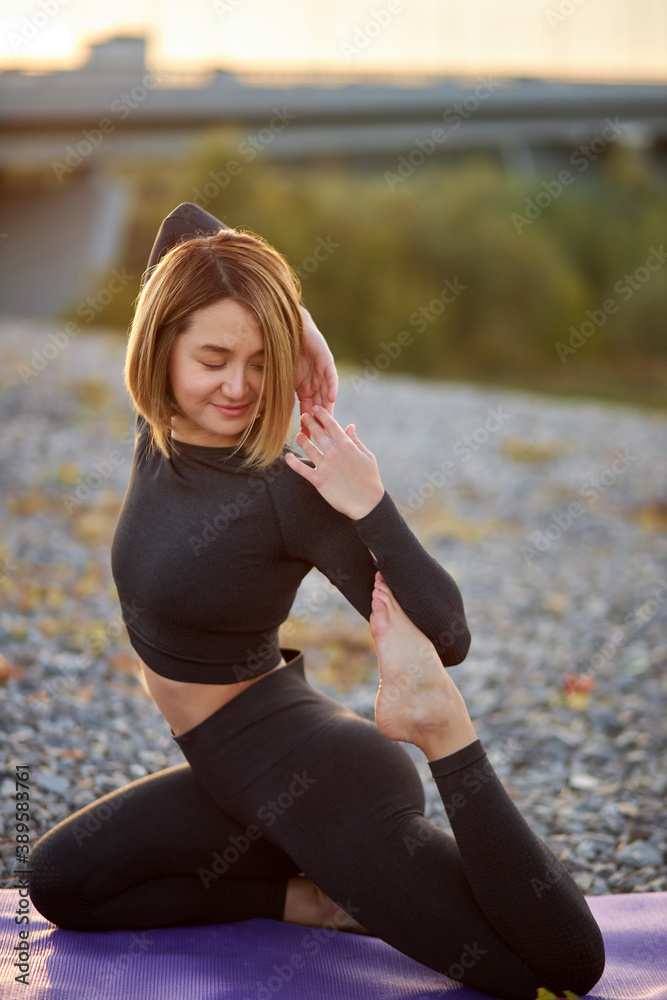 sporty beautiful woman doing yoga exercise to develop flexibility on mat outdoors, caucasian female in top and leggins