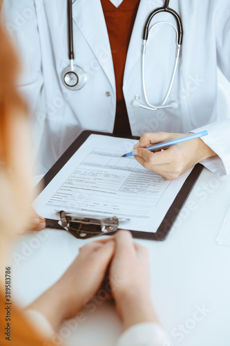 Unknown woman-doctor filling up an application form while consulting patient. Medicine concept