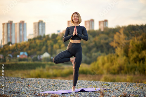 sporty fit caucasian woman doing hatha yoga asana vrikshasana tree pose outdoors, beautiful female leads healthy lifestyle, morning begins from yoga exercises