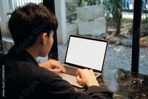 An Asian man typing a document on a white screen laptop