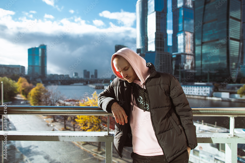 Handsome casual man in black jacket and pink hoody standing on a skyscraper view. Thinking concept