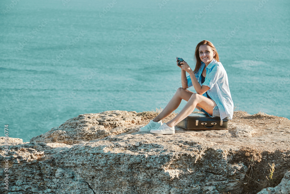 Smiling lady resting on nature sitting on luggage. Alone time near sea. Relax time and vacation abroad idea, copy space