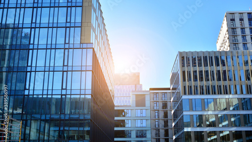 Blue curtain wall made of toned glass and steel constructions under blue sky. A fragment of a building. Glass facades on a bright sunny day with sunbeams in the blue sky.