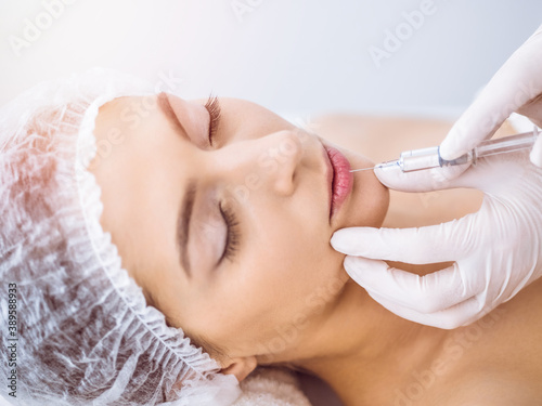 Beautician doing beauty procedure with syringe to face of young brunette woman in sunny spa center. Cosmetic medicine and surgery, beauty injections