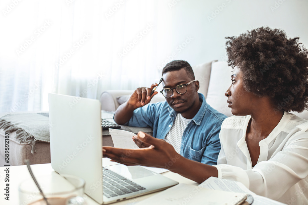 Fototapeta premium Serious African American couple discussing paper documents, sitting together on couch at home, man and woman checking bills, bank account balance, terms of contract, mortgage, loan agreement