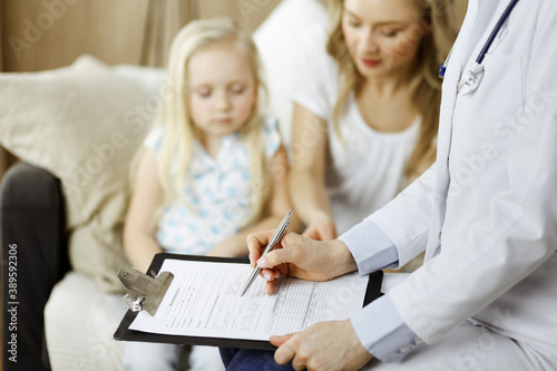 Doctor and patient. Pediatrician using clipboard while examining little girl with her mother at home. Sick and unhappy child at medical exam. Medicine concept