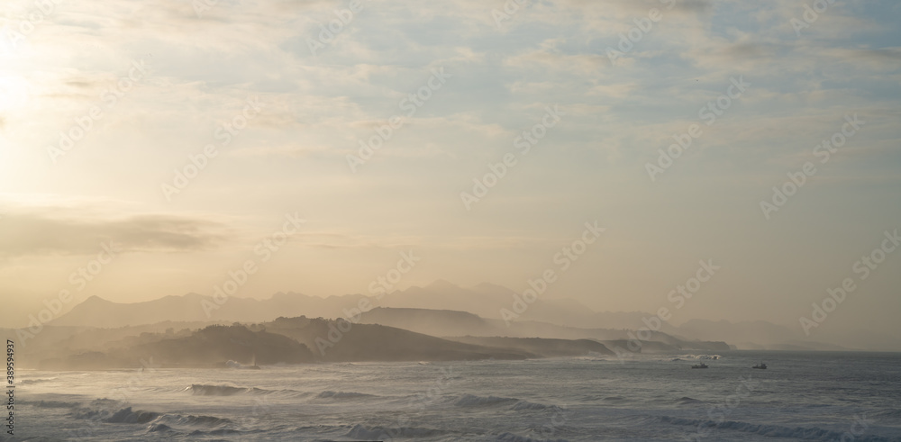 ocean coast at sunset with waves breaking and mountains in silhouette behind