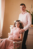 pregnant woman in a pink dress sitting in a chair behind a smiling man standing. expecting a baby