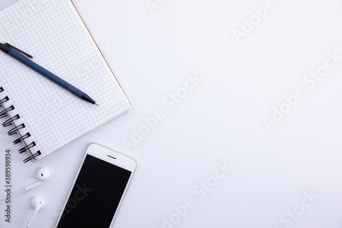 new modern smartphone with earphones and notebook isolated on white background, close view . High quality photo